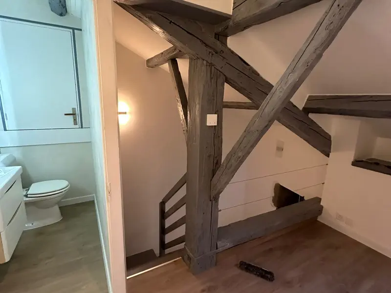 Appartement sous charpente rénové par Fred : poutres apparentes, murs blancs et sol en bois